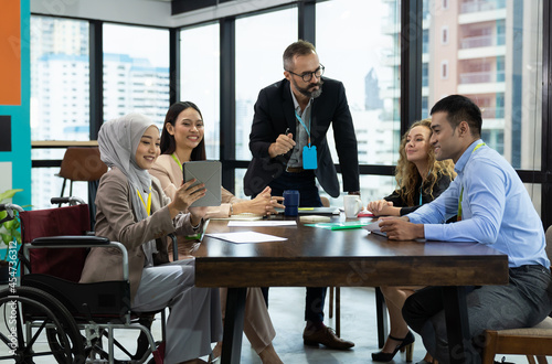 Asian Muslim business woman in hijab headscarf sitting on wheelchair presenting of her work to corporate colleagues in meeting in the modern office Poster Mural XXL