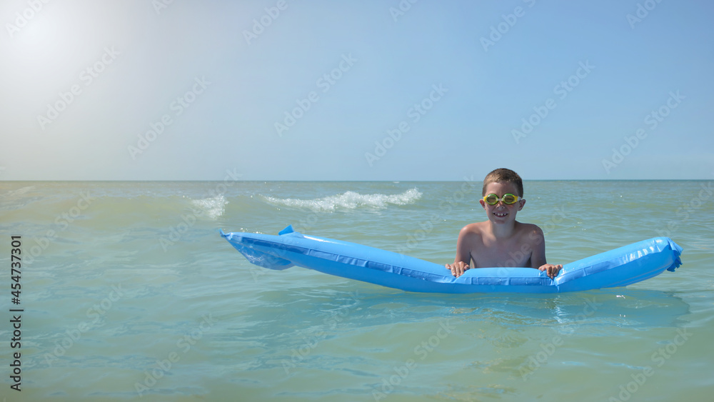 boy on an inflatable mattress in the water. joyful child spends summer vacation at the sea on a sunny day.