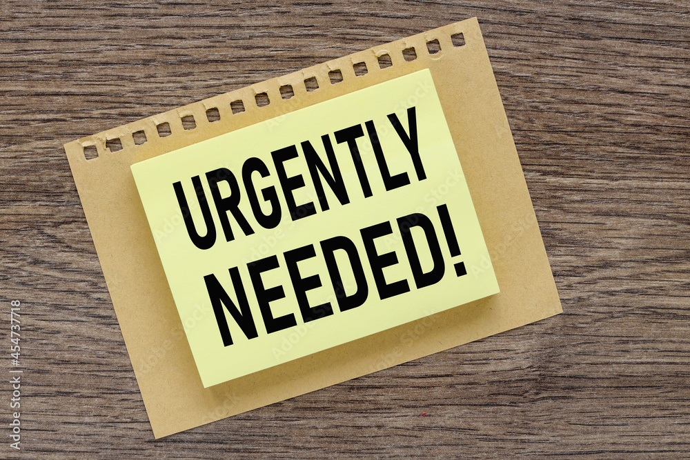 Obraz premium Urgently Needed. text on a wooden table, on a bright sticker