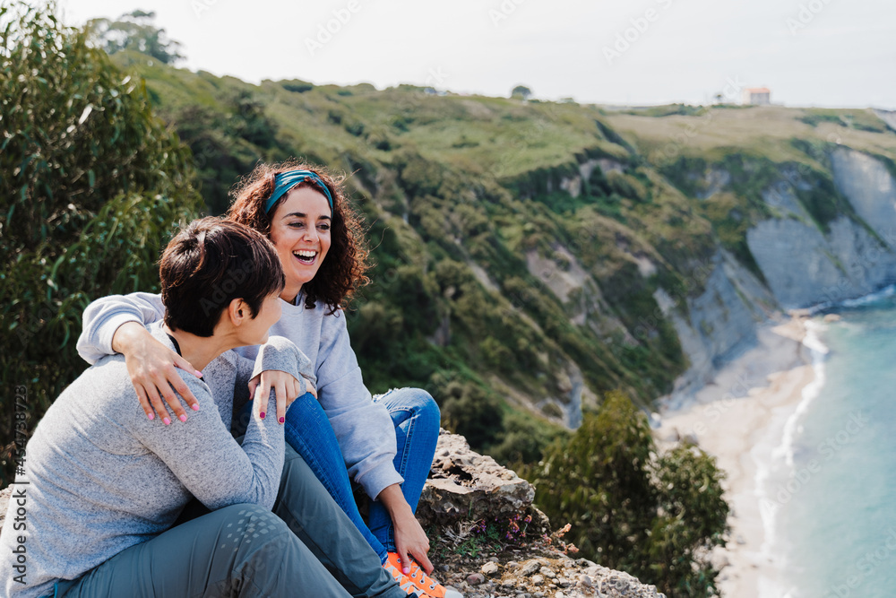 two women friends sitting, laughing and looking at beautiful sea landscape on top of the mountain. Friendship and nature concept two women friends sitting, laughing and looking at beautiful sea landscape on top of the mountain. Friendship and nature concept