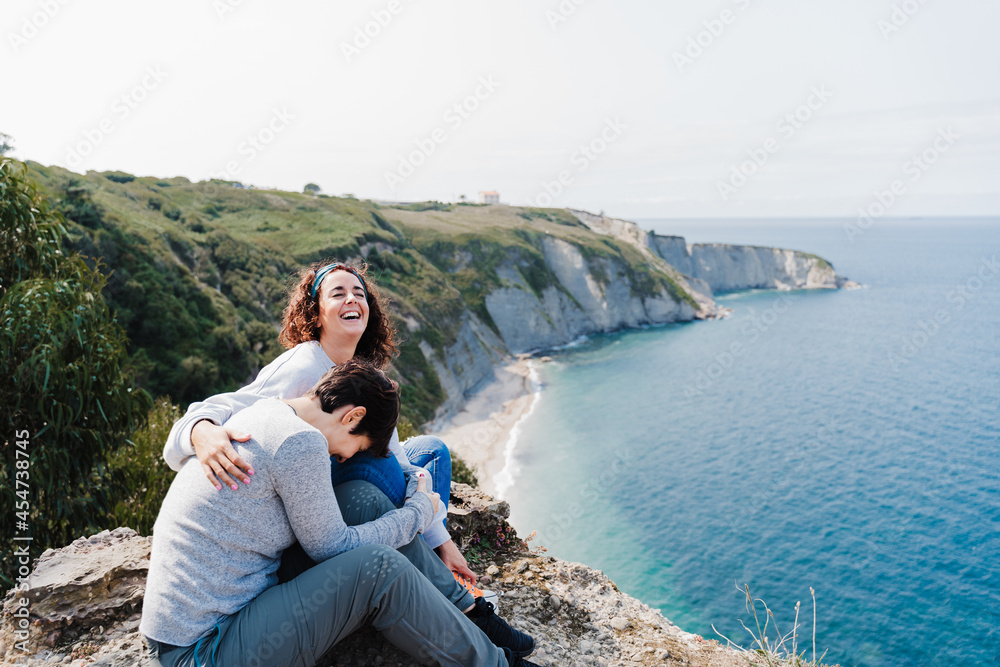 happy two women friends sitting and looking at beautiful sea landscape on top of the mountain. Friendship and nature concept