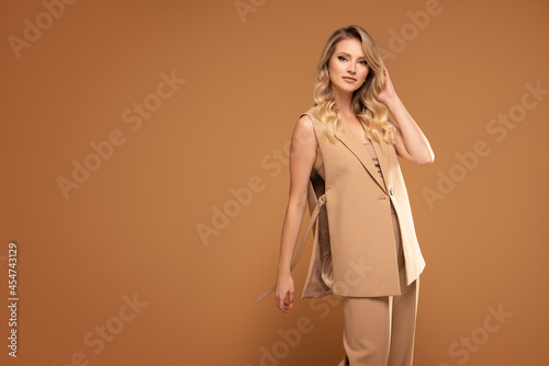Fashion studio shot of a blonde model woman in a suit isolated at the brown studio background.