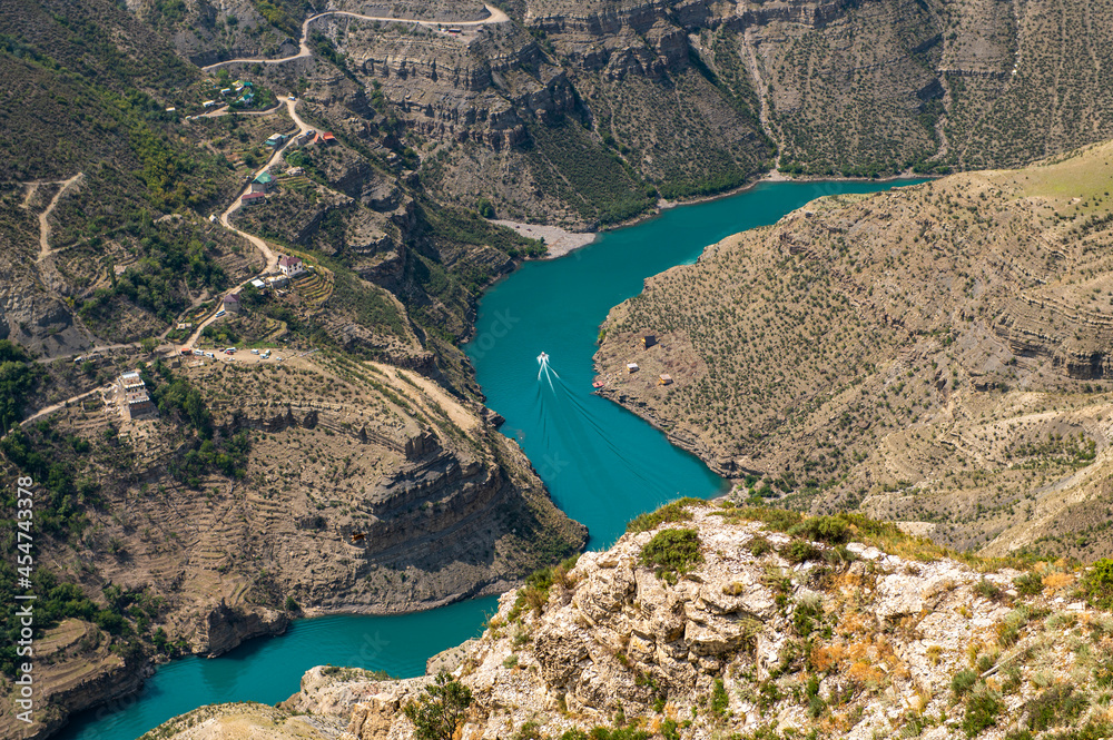 The boat sails along the blue-green Sulak River on a clear sunny day. Sulak Canyon is one of the deepest canyons in the world and the deepest in Europe. Dagestan, Russia.