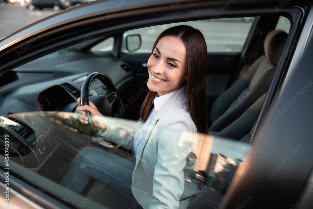 Beautiful happy successful businesswoman is driving a new modern car in good mood. Portrait cute female driver steering car with safety belt