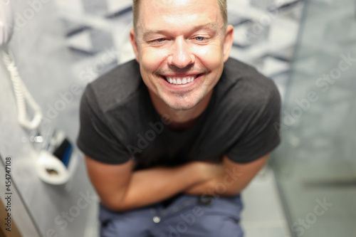 Young happy man sitting on toilet and smiling