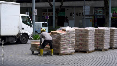 SINGAPORE, SINGAPORE - Aug 31, 2021: One construction worker moving cement bags, downtown Singapore. Locked off shot photo