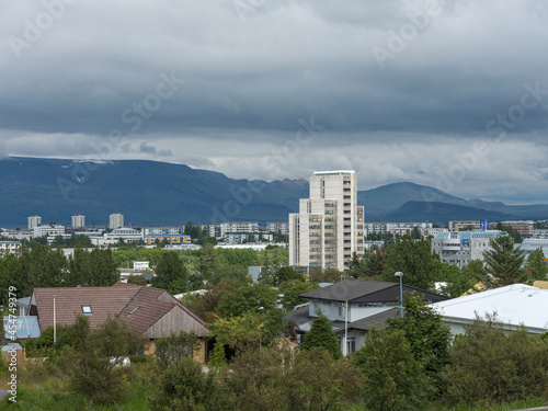 City view of Reykjavik, Iceland...Trees in between the houses and some above.  Mount. Esja in the background.  Cloudy sky.
