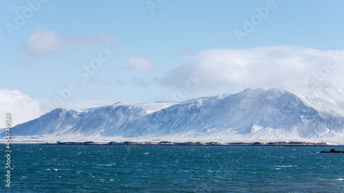 Cold day in Iceland, mt. Esja with snowy slopes and wind hitting the waves of the sea.
