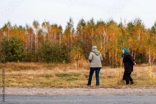 Defocus rear view of two woman on a walk in autumn nature. Fall background. Two women walking along the road in the autumn forest. Back view. Out of focus