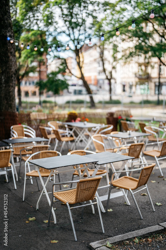 Chairs and tables in an outdoor restaurant with colourful light bulbs between trees