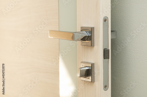 Contemporary opened door with a glass stripe with a nickel-plated handle and a latch with sun beam