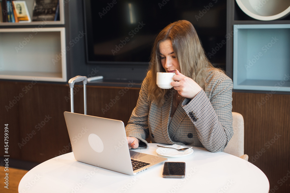 a young attractive plump girl is sitting in a cafe drinking coffee and working on a laptop