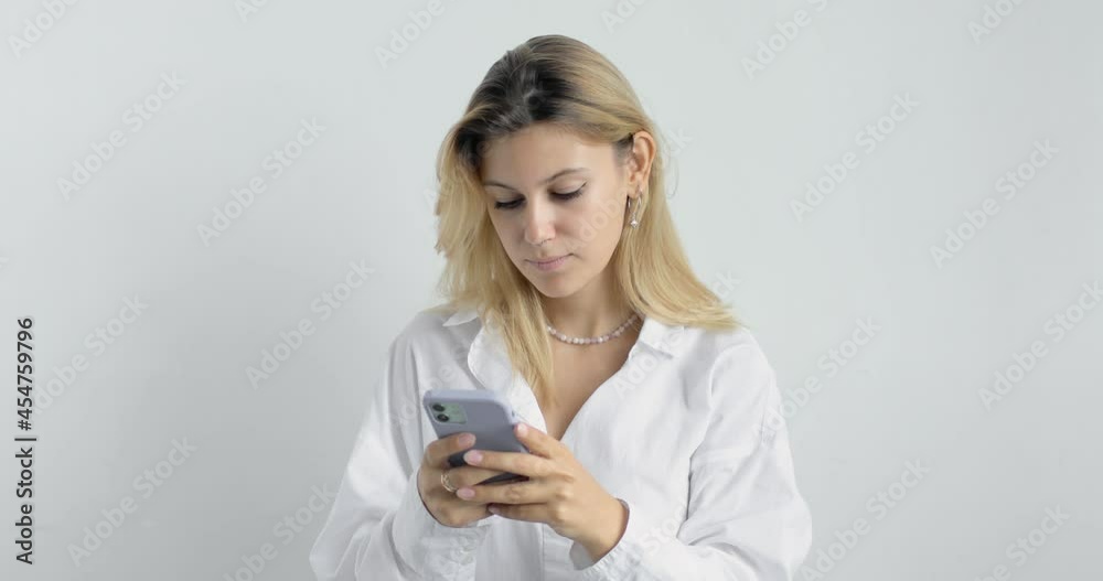 Portrait of young beautiful pensive woman in white shirt with blond hair posing isolated on white studio background. Using a mobile phone, typing, browsing the pages. People lifestyle concept. Portrait of young beautiful pensive woman in white shirt with blond hair posing isolated on white studio background. Using a mobile phone, typing, browsing the pages. People lifestyle concept.