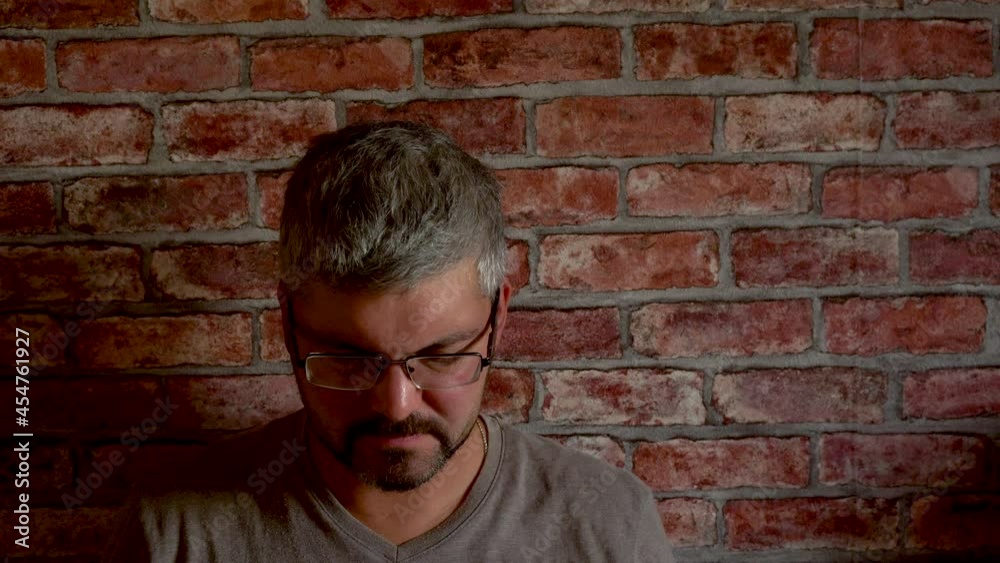 A man with a beard sits against a brick wall. Sad face. Business problems. Loss of a loved one. He dropped his head. Grey hair. Adult. Close-up. A man with a beard sits against a brick wall. Sad face. Business problems. Loss of a loved one. He dropped his head. Grey hair. Adult. Close-up.