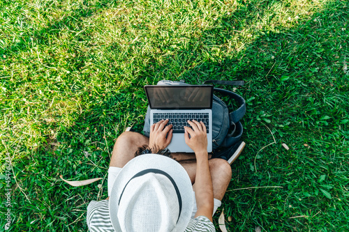 Top view of an unrecognizable young white digital nomad working remotely on a laptop sitting on a lawn photo