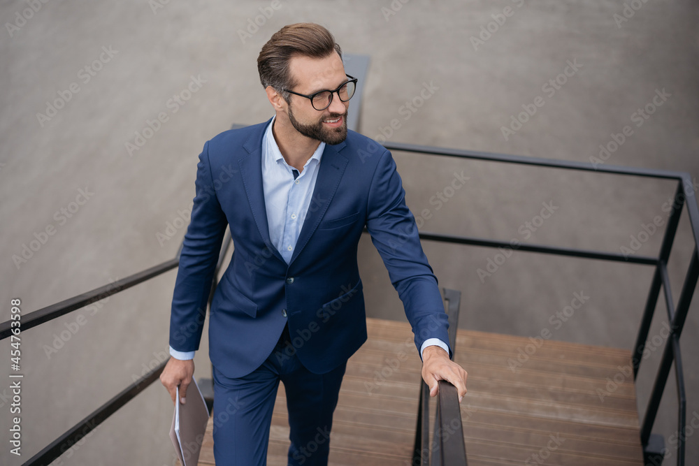 Young confident businessman holding financial documents walking up stairs looking away at copy space. Successful business, career concept Young confident businessman holding financial documents walking up stairs looking away at copy space. Successful business, career concept