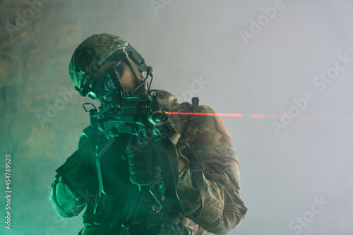Portrait of airsoft player in professional equipment with machine gun in abandoned ruined building. Soldier with weapons at war in smoke and fog