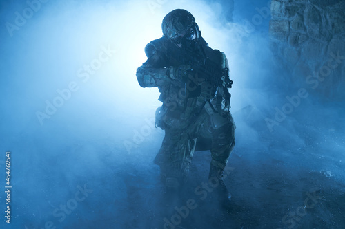 Portrait of airsoft player in professional equipment with machine gun in abandoned ruined building. Soldier with weapons at war in smoke and fog