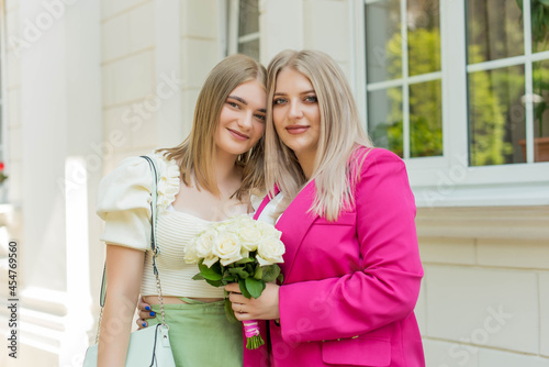 Young woman with blond hair in pink suit and smiling woman or girl with bouquet of flowers in hand happily looking at each other on wedding ceremony © MartaKlos