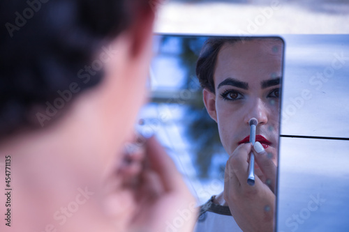 Young adult Hispanic transsexual girl doing her makeup in front of a hand mirror. Concept of transsexuality, inclusion and diversity. photo