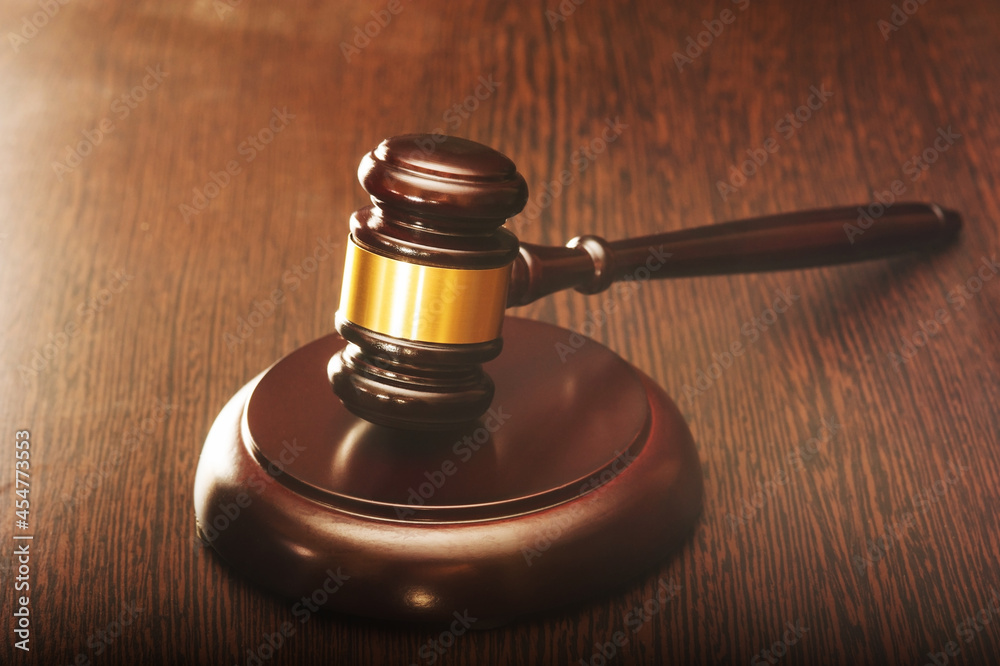 A wooden judge's hammer with a metal ring and a soundboard on a brown wooden table with a light. The concept of judging, justice.
