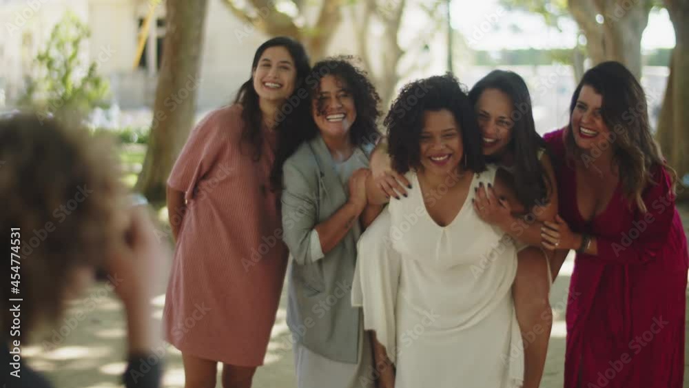 Female couple having fun and taking wedding photo with friends. Afro-American bride lifting her girlfriend on back, laughing, posing and mugging for camera. Photoshoot, LGBT wedding concept Female couple having fun and taking wedding photo with friends. Afro-American bride lifting her girlfriend on back, laughing, posing and mugging for camera. Photoshoot, LGBT wedding concept