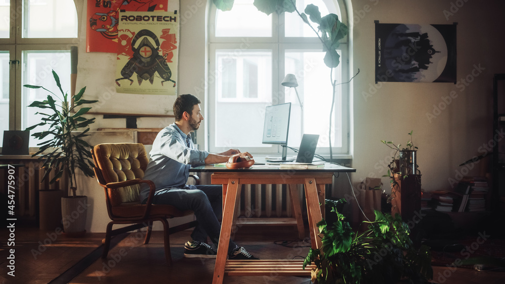 Young Handsome Man Works on a Desktop Computer in Creative Agency in Authentic Loft Office. Renovated Stylish Design with House Plants, Artistic Posters and Big Rounded Windows.