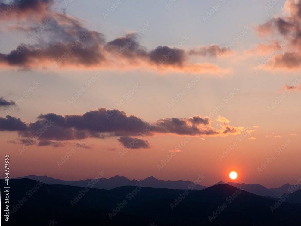 Sun setting over the peaks of the rocky mountains with pastel colored sky and pretty clouds.