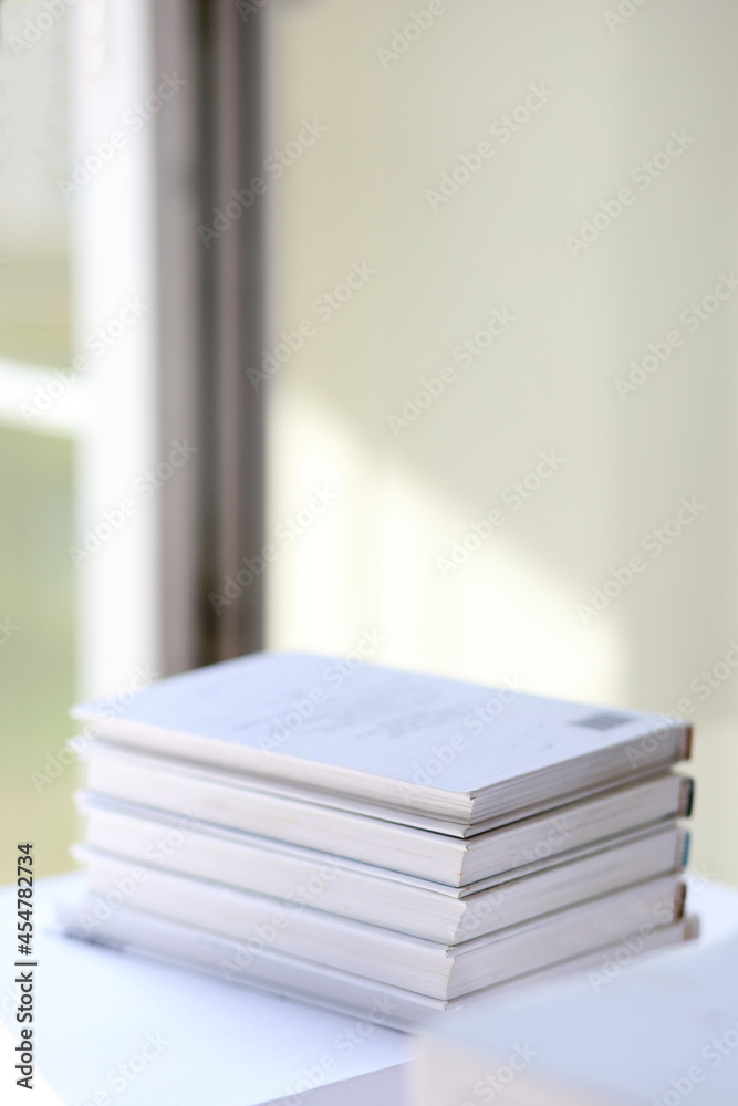 Stacked books vertical stock photography with opened window and sun light on the wall.