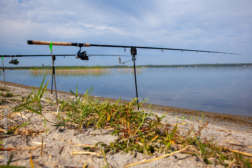 Two fishing rods on a stand with electronic bite alarm on the shore on a sunny summer day. Fishing bite alarm.