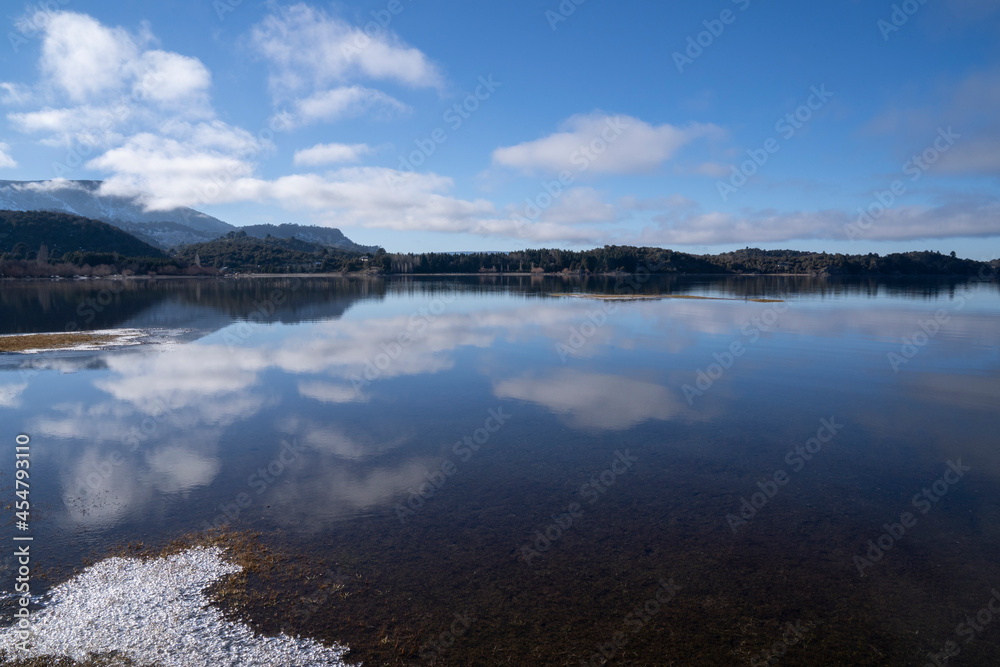 The calm lake in a sunny morning. Panorama view of the forest, lake and the perfect reflection of the sky in the blue water. The Andes mountain range in the background.