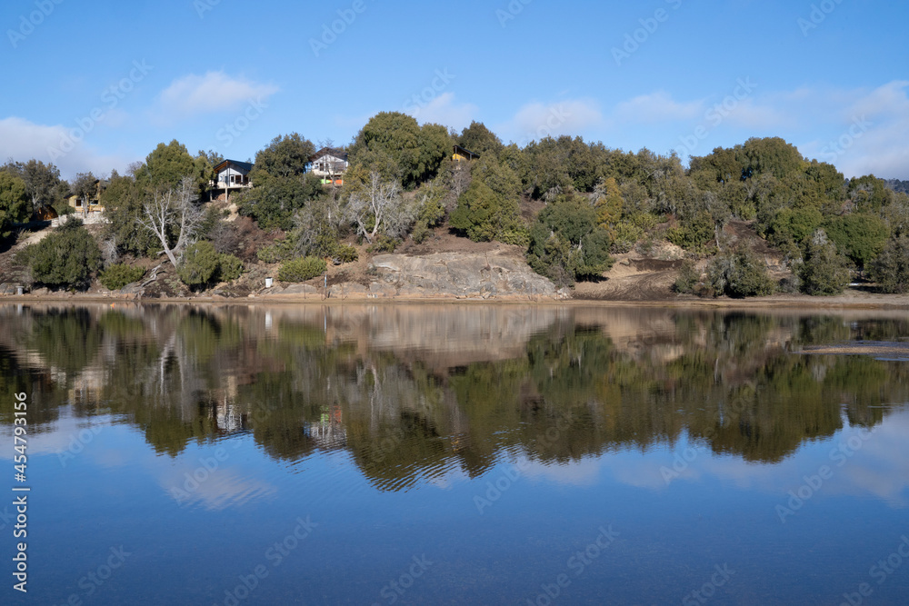Panorama view of the wooden lake houses in the forest. The shoreline, wood, cliffs, and blue sky reflection in the water. Panorama view of the wooden lake houses in the forest. The shoreline, wood, cliffs, and blue sky reflection in the water.
