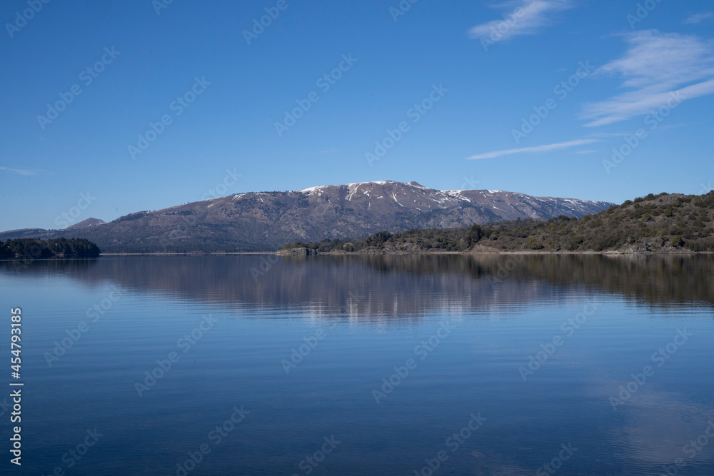 The lake in a sunny morning. Panorama view of the forest, lake and the perfect reflection of the sky in the blue water. The Andes mountain range in the background.