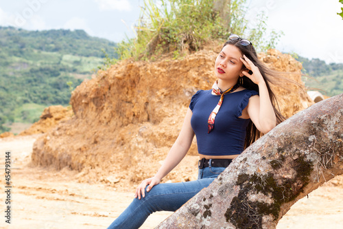 Young Latin American girl in profile. posing on a log in a natural landscape. In one-piece outdoors