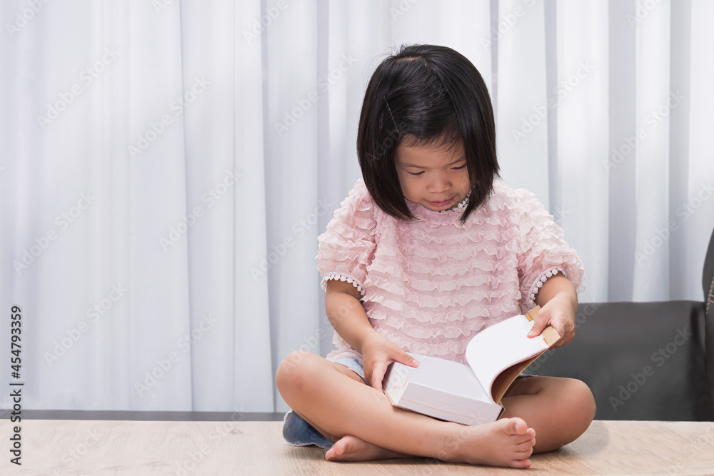 Asian child sitting and reading big book on wood table in her house. Happy girl sweet smile. Kid was amazed by the new book she was holding. Children aged 4-5 years old. Asian child sitting and reading big book on wood table in her house. Happy girl sweet smile. Kid was amazed by the new book she was holding. Children aged 4-5 years old.