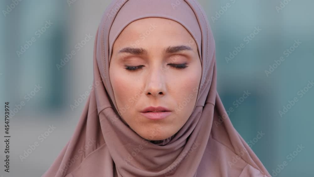 Close-up serious female face portrait outdoors young muslim islamic woman in hijab stands on street looking at camera holds index finger near mouth makes silence gesture hush secrets forbids speaking Close-up serious female face portrait outdoors young muslim islamic woman in hijab stands on street looking at camera holds index finger near mouth makes silence gesture hush secrets forbids speaking