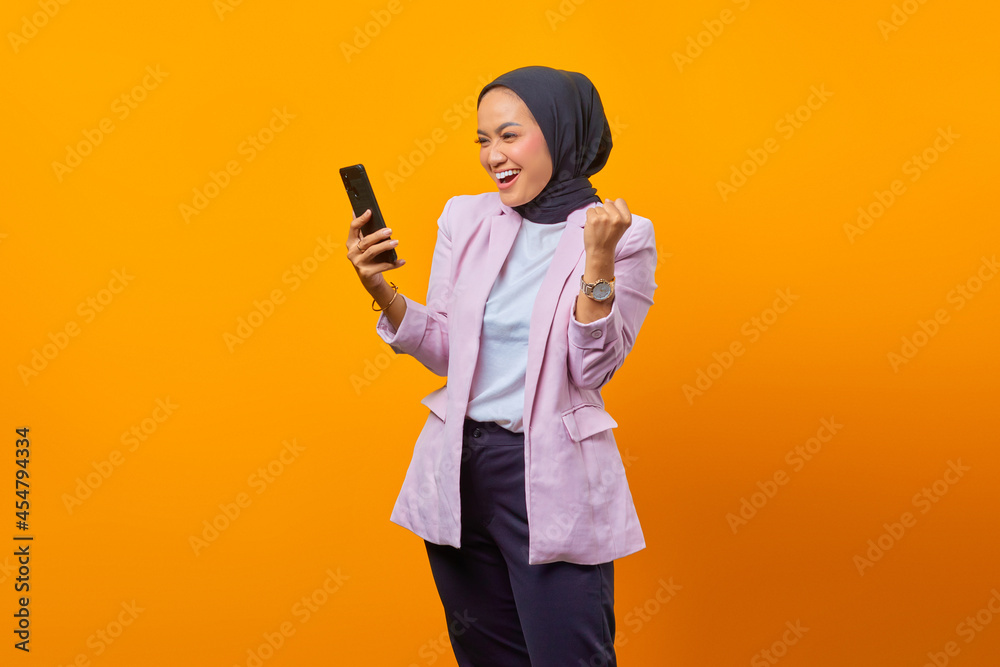 Cheerful asian woman showing smartphone blank screen and celebrating success isolated on yellow background Cheerful asian woman showing smartphone blank screen and celebrating success isolated on yellow background