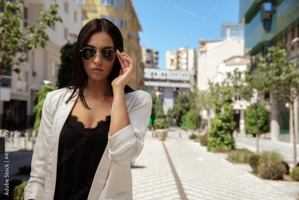 Close up image of happy brunette woman in sunglasses and summer clothes posing sideways outdoors