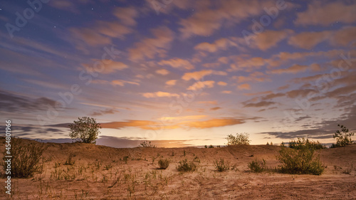 Shining bright clouds and sandy landscape with starry sky at sunrise