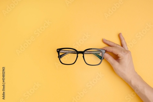 Hand holding black eyeglasses on yellow background. Flatlay