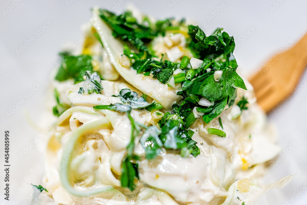 Closeup of shredded spiralized zucchini uncooked raw noodles pasta for raw vegan cooking preparation or low-carb substitution of fettuccine creamy Italian zoodles dish with green parsley herb