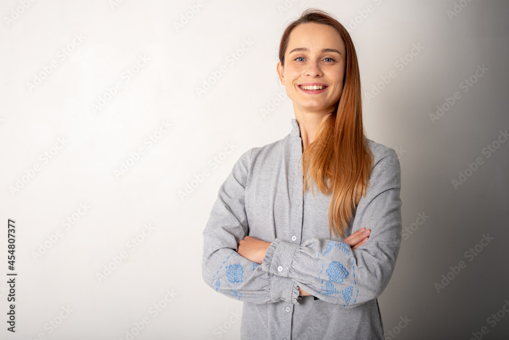 Confident woman in light gray clothes with blue eyes, blond hair and a smile on her face looks at the camera, standing by the white wall with her arms crossed. People, youth, beauty, lifestyle concept Confident woman in light gray clothes with blue eyes, blond hair and a smile on her face looks at the camera, standing by the white wall with her arms crossed. People, youth, beauty, lifestyle concept