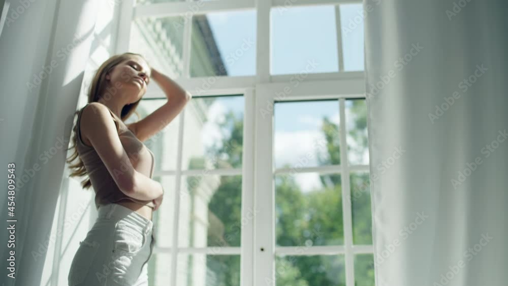 Beautiful girl - model looks out the window, then straightens her hair. Medium shot with radial camera movement. A young girl watching a sunny day Beautiful girl - model looks out the window, then straightens her hair. Medium shot with radial camera movement. A young girl watching a sunny day