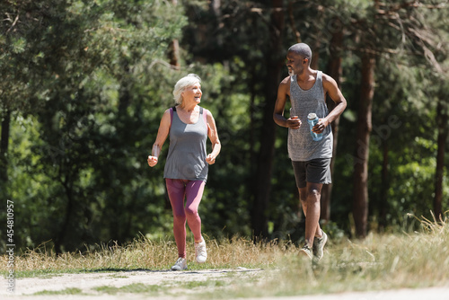 African american sportsman running near cheerful senior wife in forest.