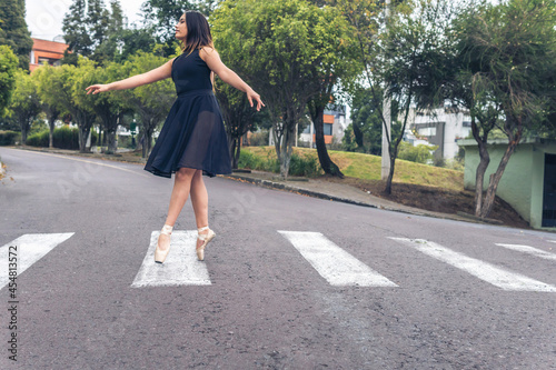 Latin teenage dancer girl with black dress walking elegantly with ballet shoes on a pedestrian crossing in the street