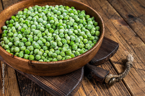 Cold Frozen green peas in a wooden plate. Wooden background. Top view