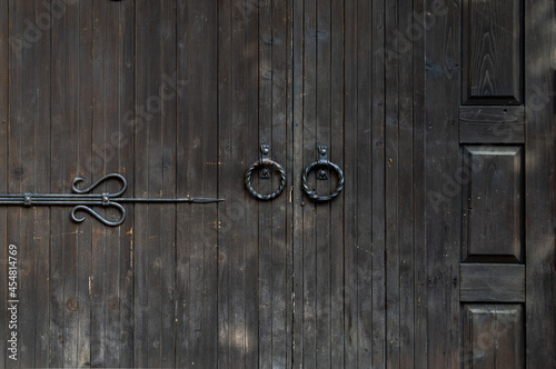 Old wooden doors with round forged handles. Plane rusted wooden door. Forged staff elements.