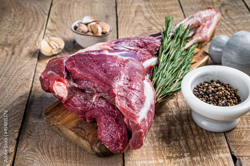 Raw lamb mutton leg with rosemary and pepper on cutting board. wooden background. Top view. Copy space.