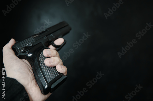 Firearm in man's hand. First person view of gun. Criminal with pistol on black background. Defense or attack. Murderer or armed thief. Close up with copy space.