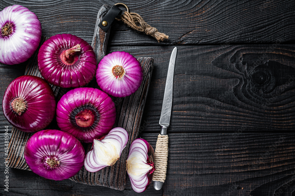 Whole and halfed Flat red sweet onion on a cutting board. Black Wooden background. Top View. Copy space